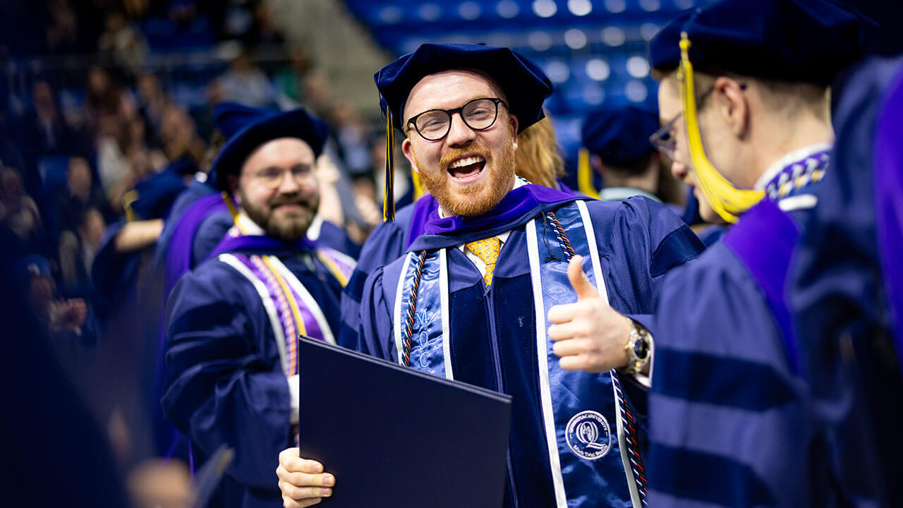 A graduate smiles and gives a thumbs up