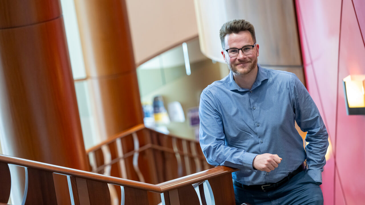 Headshot of Bill Ollayos inside on a staircase, plays video